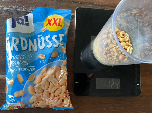 Ein Beispiel: Einer Gruppe steht eine Packung mit 500g Erdnüssen zur Verfügung. Auf der Feier soll damit an vier verschiedenen Stellen eine Schachtel bereitgestellt werden, demnach beträgt eine Portion 125 g. Diese abgewogene Menge an Erdnüssen ergibt in einem Messbecher ein Volumen von 200 ml. Die Gruppe entscheidet sich für eine sehr flache Schachtel mit einer Höhe von 2 cm, die jeweils bis zum Rand gefüllt werden soll.